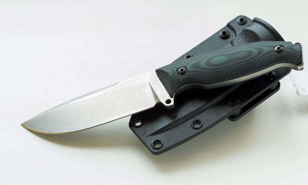 A knife with a custom green wood-grain handle lying on top of its sheath. The sheath is black and lying against a white background.