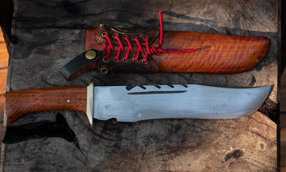 A large knife lying on a wooden bench next to its sheath. This knife is likely used for big game hunting.