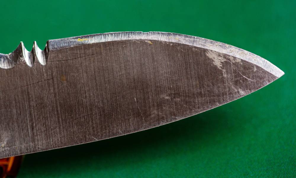 A close-up of a dull knife that has a couple of nicks and scratches. The knife is in front of a green background.